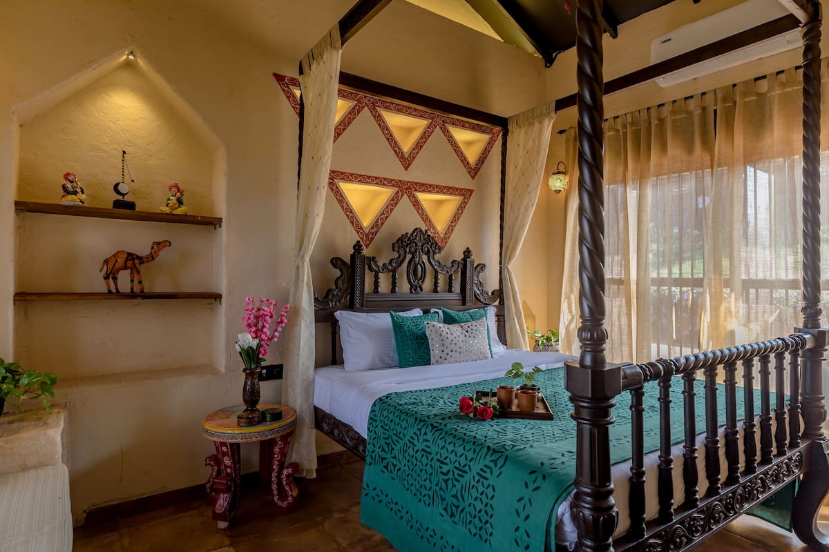 A four-poster bed with a green bedspread, a wooden headboard, and a decorative wall above.