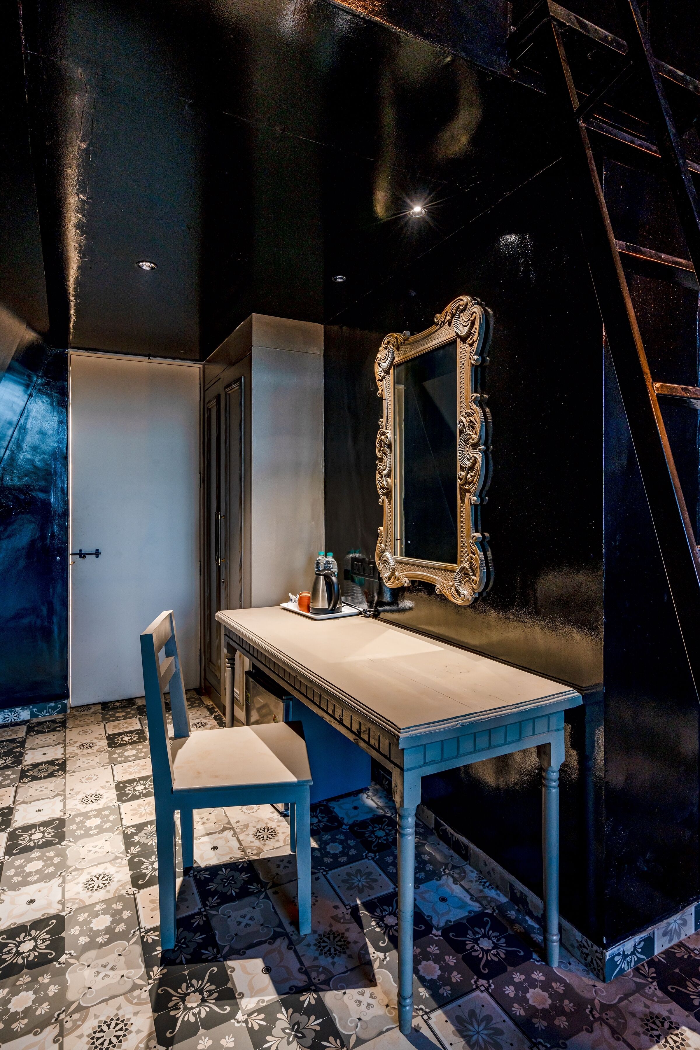 A room with a tiled floor, a wooden chair, a small table, a mirror with an ornate frame, and a ladder against the wall.