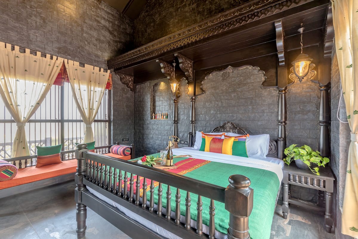 A traditional room with a bed, a window with curtains, a nightstand, and a wall-mounted light fixture.