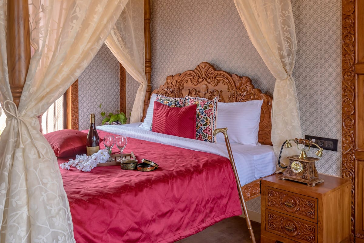 A four-poster canopy bed with a red bedspread, a bedside table with a clock, and a nightstand.