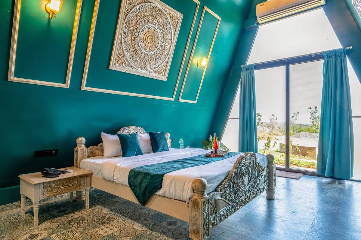 A bedroom with a large bed, a nightstand, a decorative wall panel, and a view through a large window.