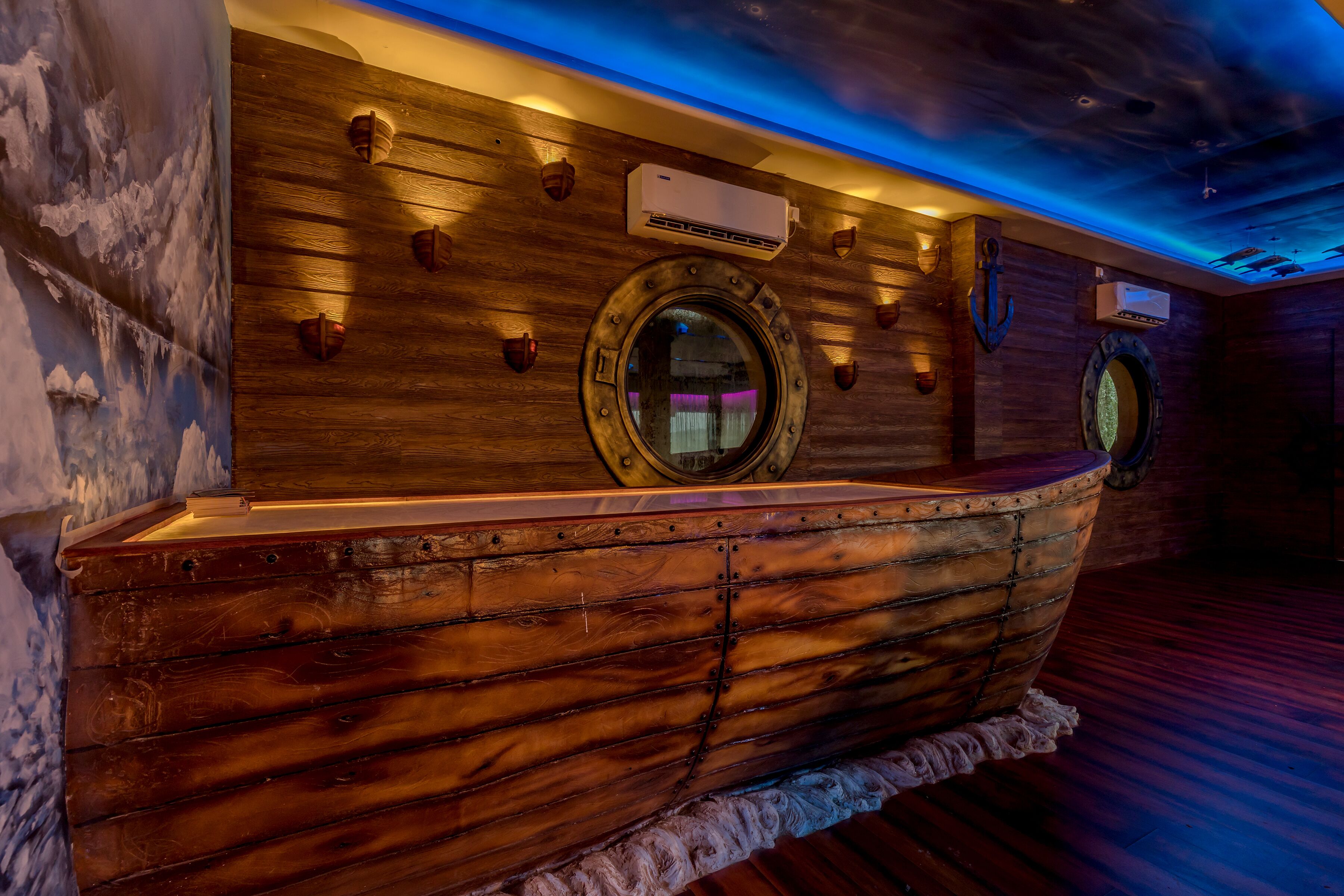 Un comptoir d’accueil en bois, en forme de bateau, doté d’une fenêtre ronde, de murs en bois et d’un plafond éclairé d’une lumière bleue.