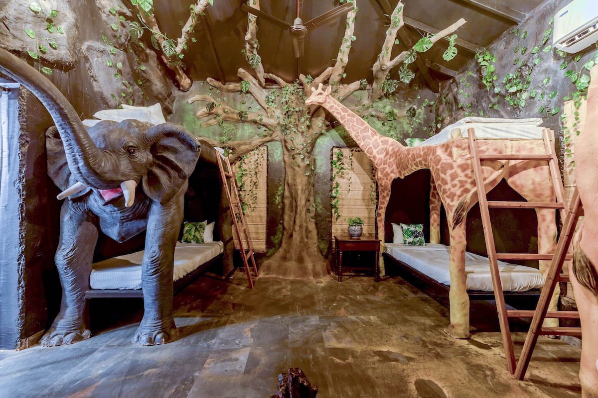 A room with a tree-themed design, including a giraffe and an elephant statue, two beds, and a ladder.