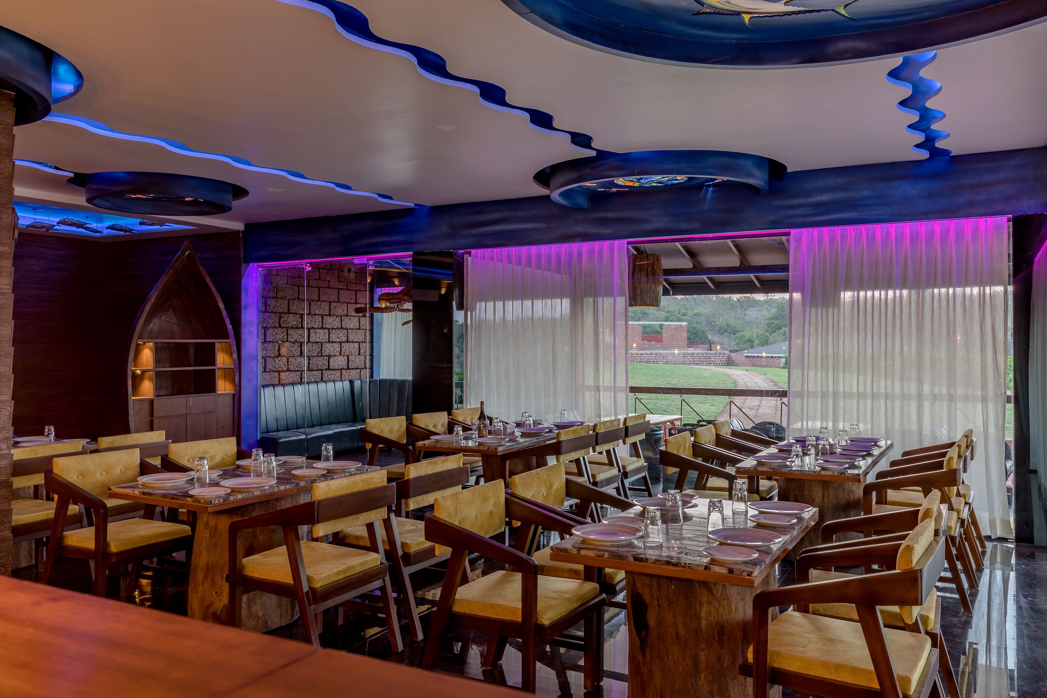 A restaurant with wooden tables and chairs, a brick wall, and a view of a field.