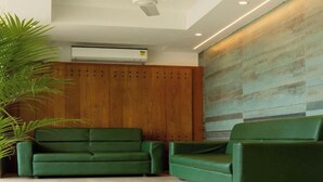 A reception area with two green sofas, a wooden panel wall, and an air conditioning unit. - Flora Pavillion Near Global Hospital Perumbakkam (Chennai)