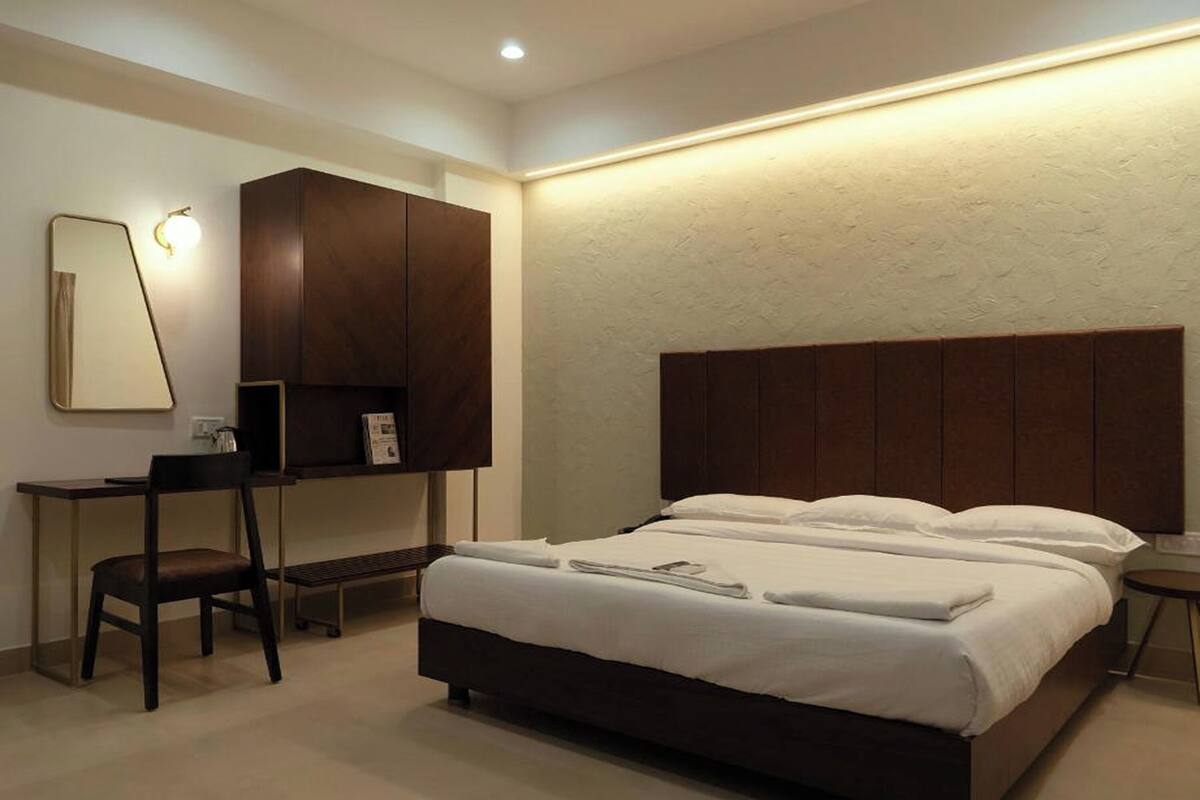 A modern hotel room with a large bed, a desk, and a wardrobe.