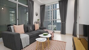 Ein modernes Wohnzimmer mit einer grauen Couch, einem kleinen weißen Tisch und einem großen Fenster mit grauen Vorhängen.