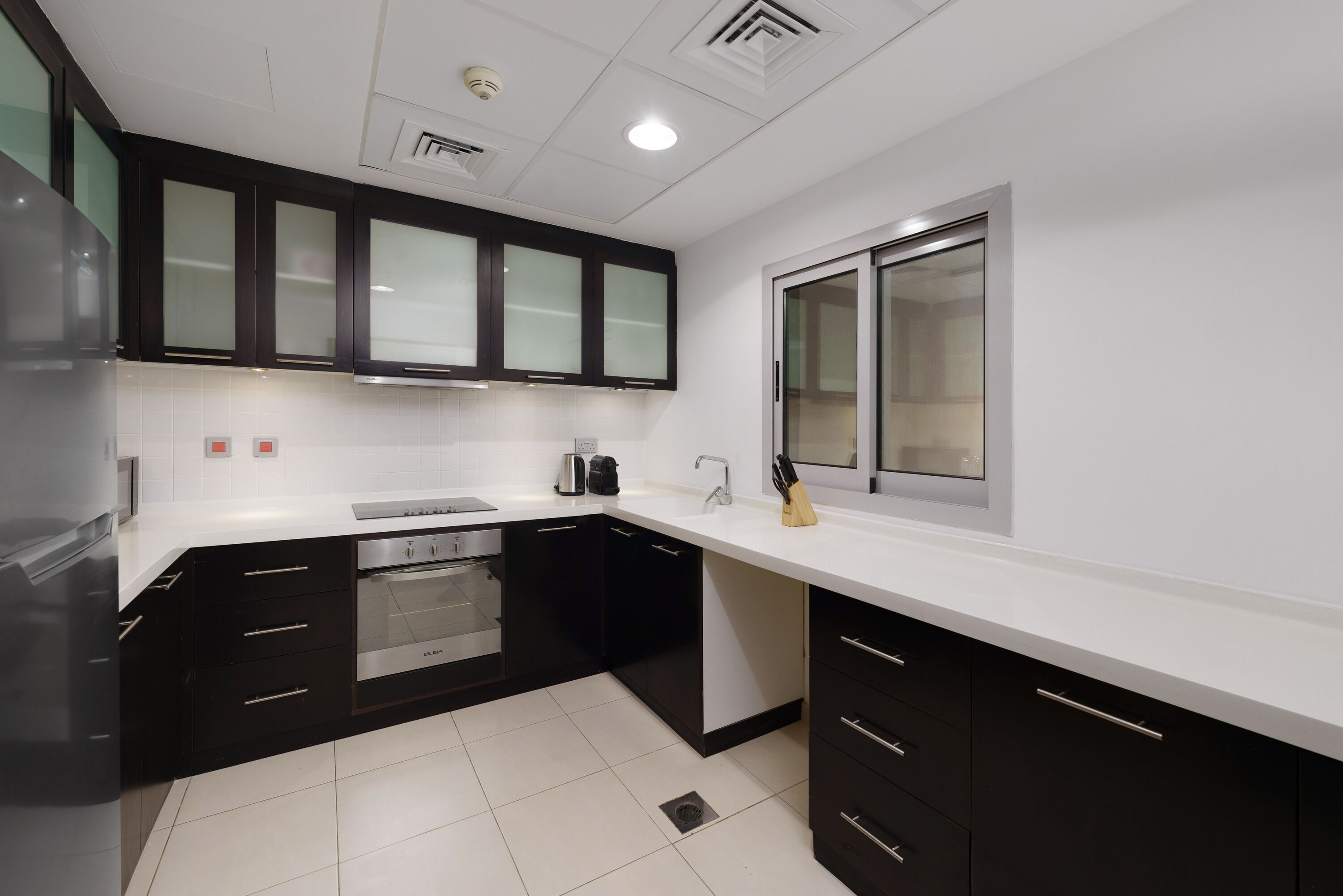 A modern kitchen with black cabinets, a white countertop, stainless steel appliances, and a window.