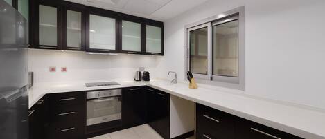 A modern kitchen with black cabinets, a white countertop, stainless steel appliances, and a window.