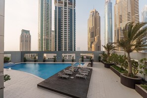 A rooftop pool area with lounge chairs and potted plants, surrounded by high-rise buildings.