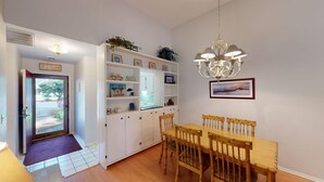 A dining area with a wooden table and chairs, a chandelier, and a white cabinet with shelves.