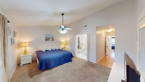 A bedroom with a bed, bedside lamps, a ceiling fan, and a bathroom visible through an open door.