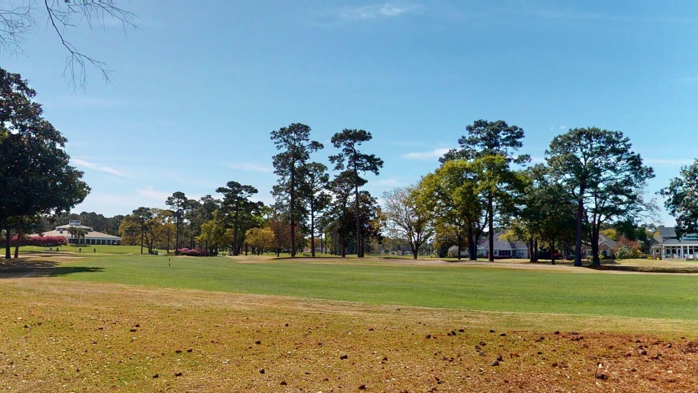 Ein Golfplatz mit Clubhaus, Bäumen und blauem Himmel.