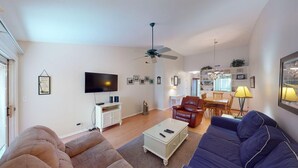 A living room with a TV, sofas, a ceiling fan, and a dining area with a table and chairs.
