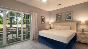 A bedroom with a large bed, a ceiling fan, a nightstand with a lamp, and a view through a sliding glass door to an outdoor area. - River Club 3 Bedroom: Golf Views  and Amenities (Pawleys Island)
