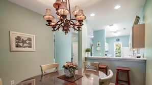 A dining area with a round table, chairs, a chandelier, and a kitchen in the background. - River Club 3 Bedroom: Golf Views  and Amenities (Pawleys Island)