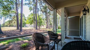 A covered porch with wicker furniture, a view of a wooded area, and a house in the background. - River Club 3 Bedroom: Golf Views  and Amenities (Pawleys Island)