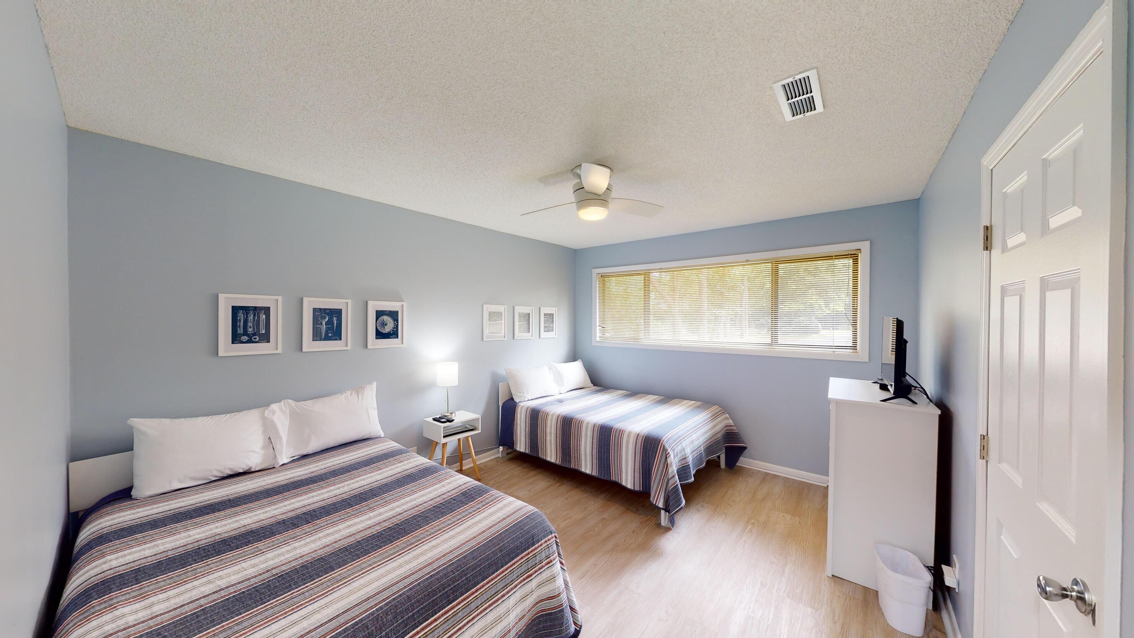 A bedroom with two beds, a ceiling fan, a window with blinds, and a door.