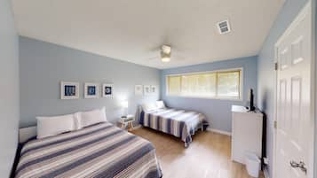 A bedroom with two beds, a ceiling fan, a window with blinds, and a door.