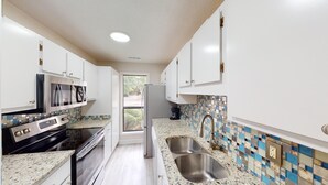Cocina moderna con armarios blancos, electrodomésticos de acero inoxidable, salpicadero de azulejos y ventana con vistas a la vegetación.