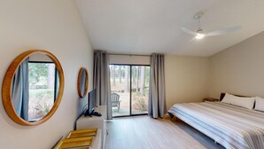 Un dormitorio con una cama, un ventilador de techo, un ventanal con cortinas y vistas a árboles.