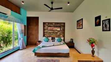 Quarto com cama grande, ventilador de teto, cabeceira de parede de pedra, mesa de cabeceira com telefone, vaso com flores e janela com cortinas.
