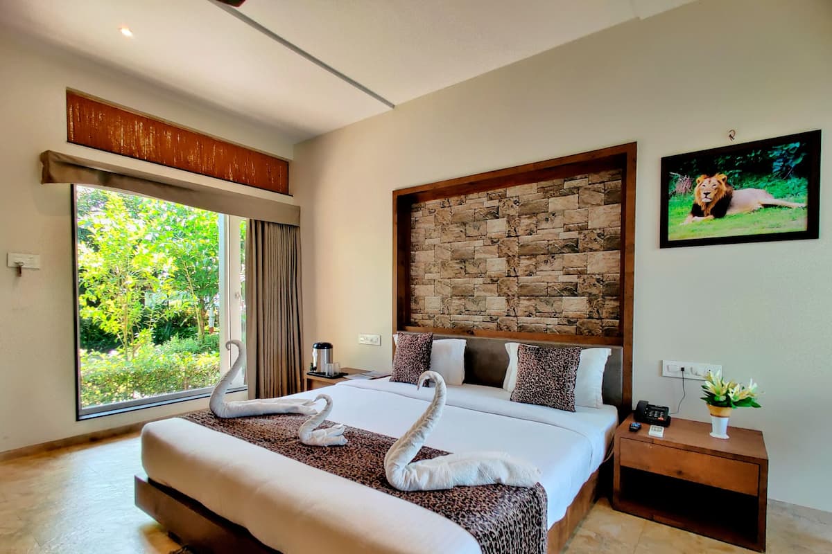 A spacious bedroom with a large bed, a stone wall headboard, and a view of greenery through a sliding door.