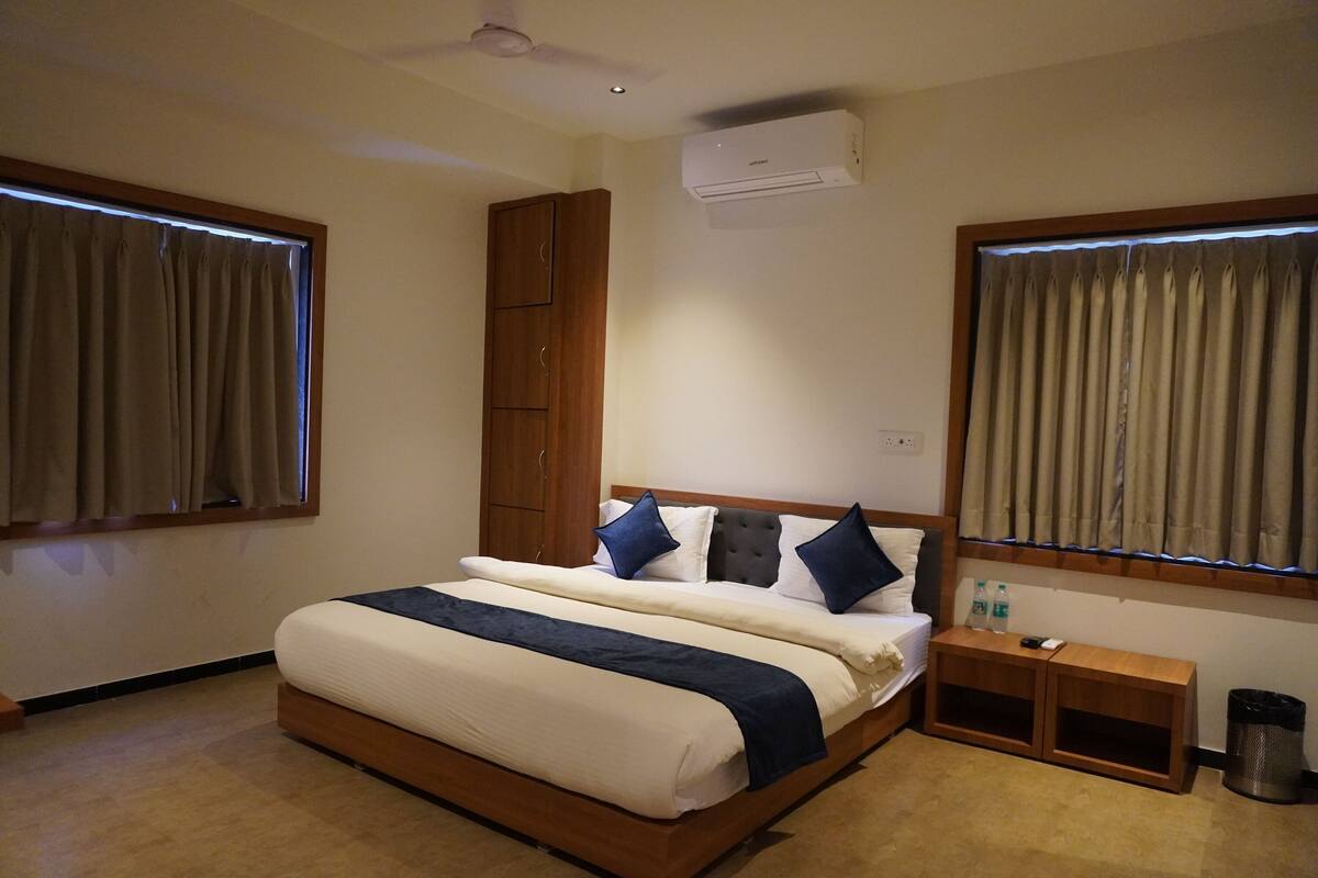 A bedroom with a large bed, wooden headboard, two bedside tables, a waste bin, and an air conditioning unit.