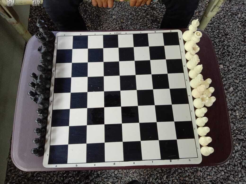 Un tablero de ajedrez con casillas negras y blancas, una mesa morada y una fila de objetos blancos a la derecha.