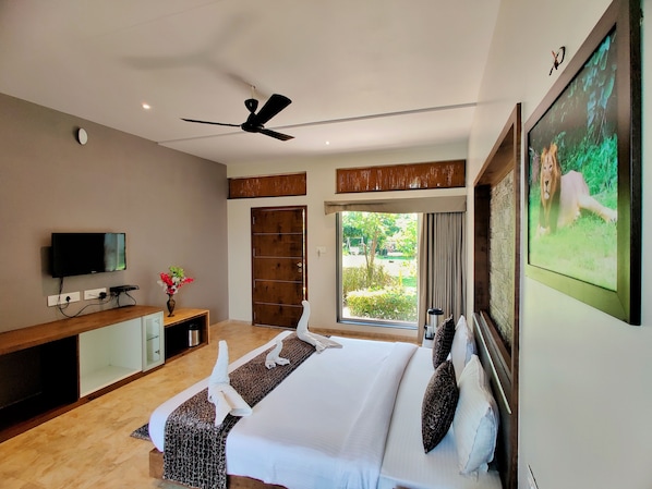A modern hotel room with a large bed, a flat-screen TV, a ceiling fan, and a large window with a view of greenery. - Lion Signature Family Resort (Talala)
