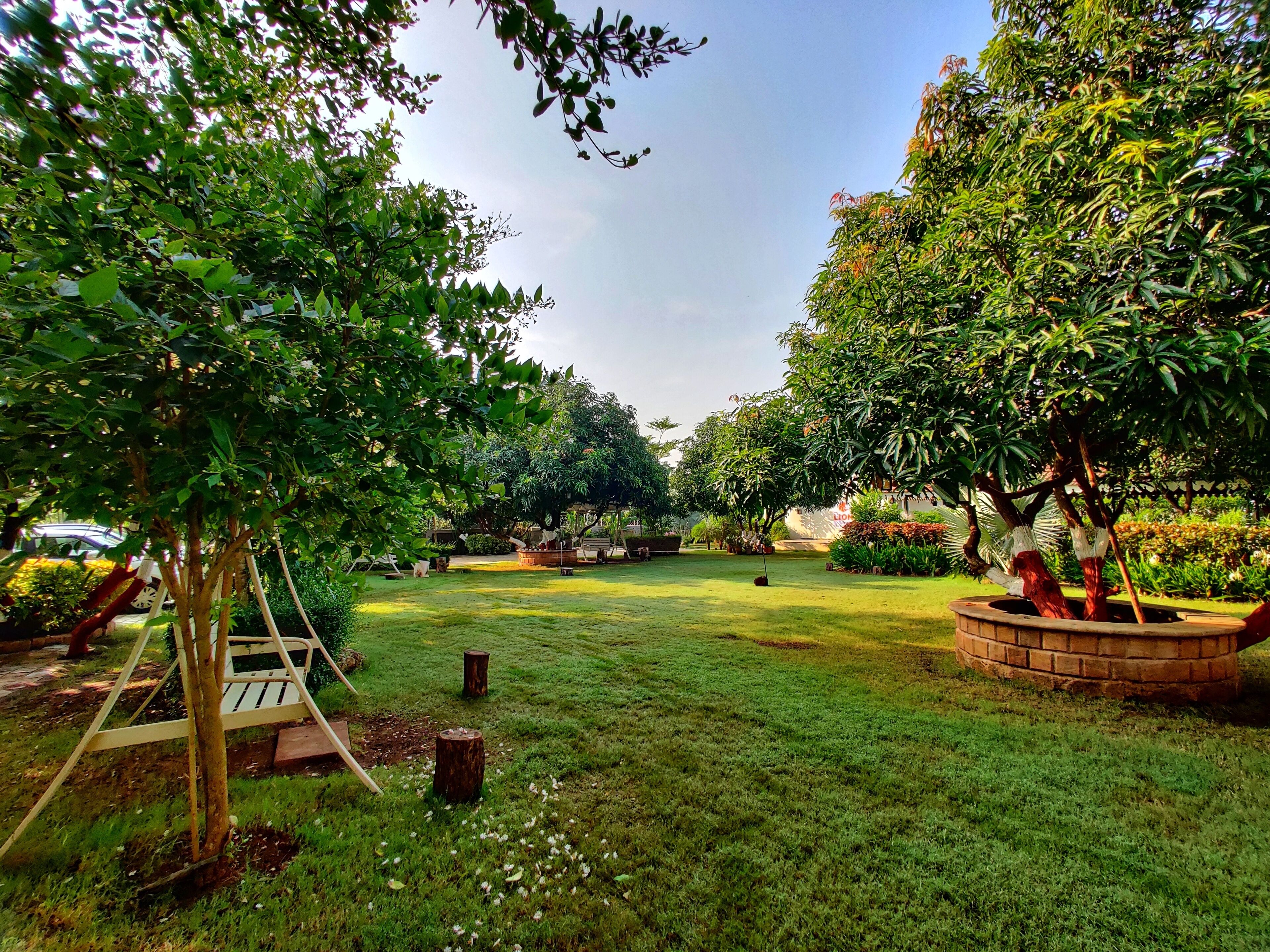 A well-maintained garden with a swing set, a brick planter, and a variety of trees and shrubs.