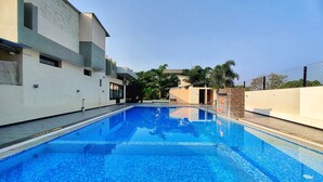 Ein Schwimmbecken mit Fliesenboden, umgeben von einem modernen Gebäude mit flachem Dach und einem kleinen Anbau mit Tür.