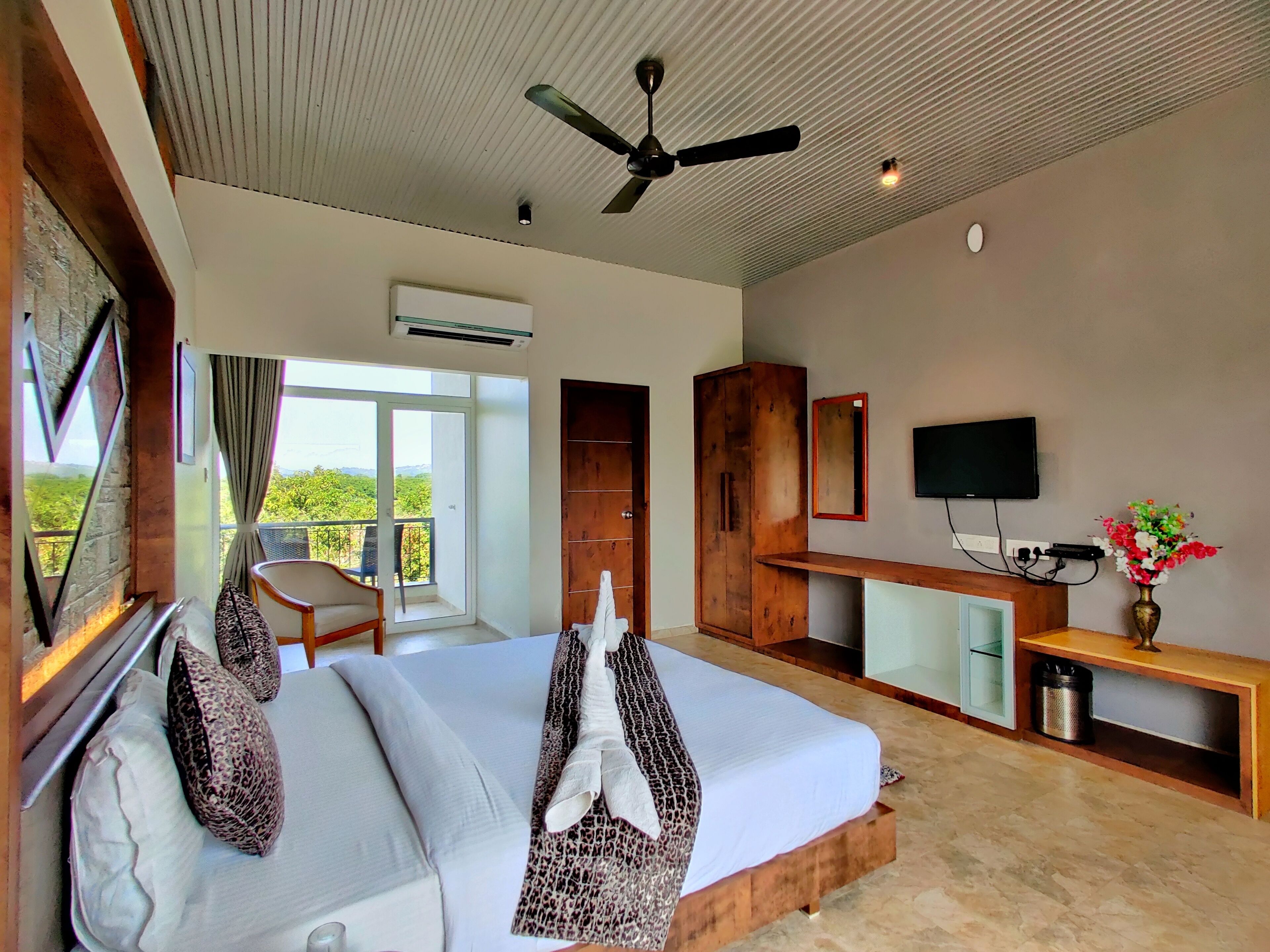 A hotel room with a bed, a desk, a TV, and a balcony with a view.