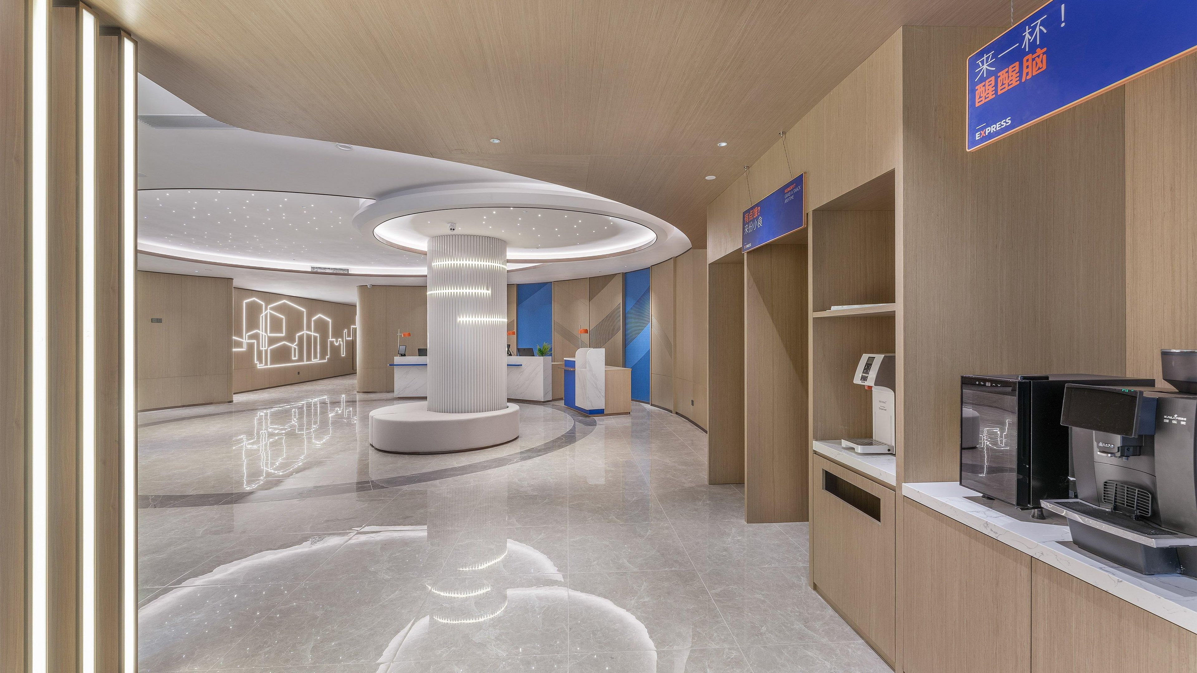 A modern hotel lobby with a reception desk, a coffee machine, and a digital screen.