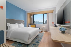 Habitación de hotel con cama, escritorio, televisor y ventana con vista a la ciudad.