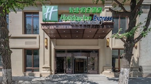 A hotel entrance with a sign for Holiday Inn Express, a covered entrance, and a large tree to the left.