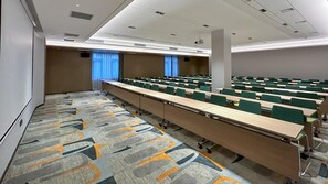 A conference room with rows of tables and chairs, a carpeted floor, and a whiteboard.