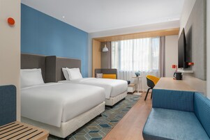 A hotel room with two beds, a sofa, a small table, a chair, a TV, and a window with curtains.