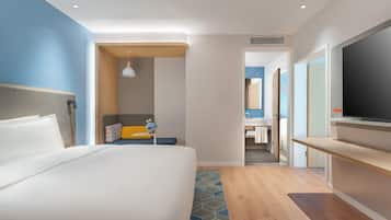 Habitación de hotel con cama, televisor, escritorio y baño visible a través de una puerta abierta.