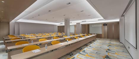 A conference room with rows of tables, chairs, and a projector screen.
