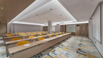 A conference room with rows of tables, chairs, and a projector screen.