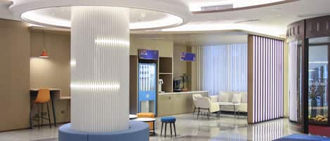 A modern lobby with a central column, seating areas, a reception desk, and a glass partition.