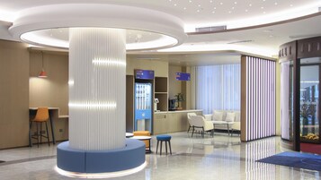 Un vestíbulo moderno con una columna central, zonas de estar, un mostrador de recepción y una pared de vidrio.