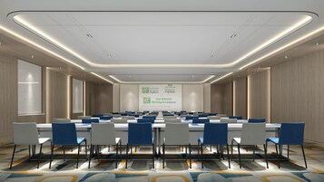 Un salón de conferencias con una pantalla grande mostrando el logotipo de Holiday Inn Express, varias mesas con sillas y una alfombra estampada.