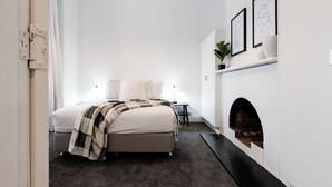 A bedroom with a bed, a fireplace, and framed artwork on the wall.