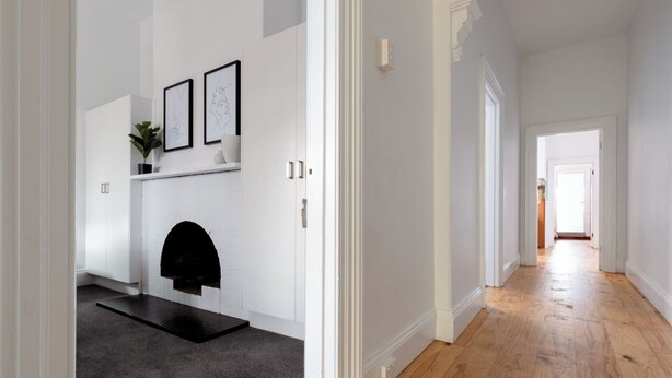 A hallway with a fireplace, white walls, and a wooden floor.