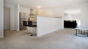 A modern kitchen with a built-in island, two bar stools, a refrigerator, and a dining table.