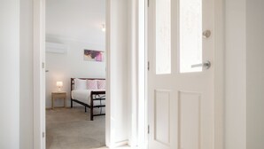 A hallway leading to a bedroom with a bed, a nightstand, and a wall-mounted lamp.