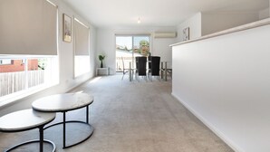A spacious room with a large window, a small round table, and a dining area with chairs.