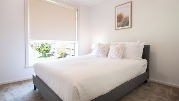A bedroom with a large bed, a window with a blind, and a framed picture on the wall.